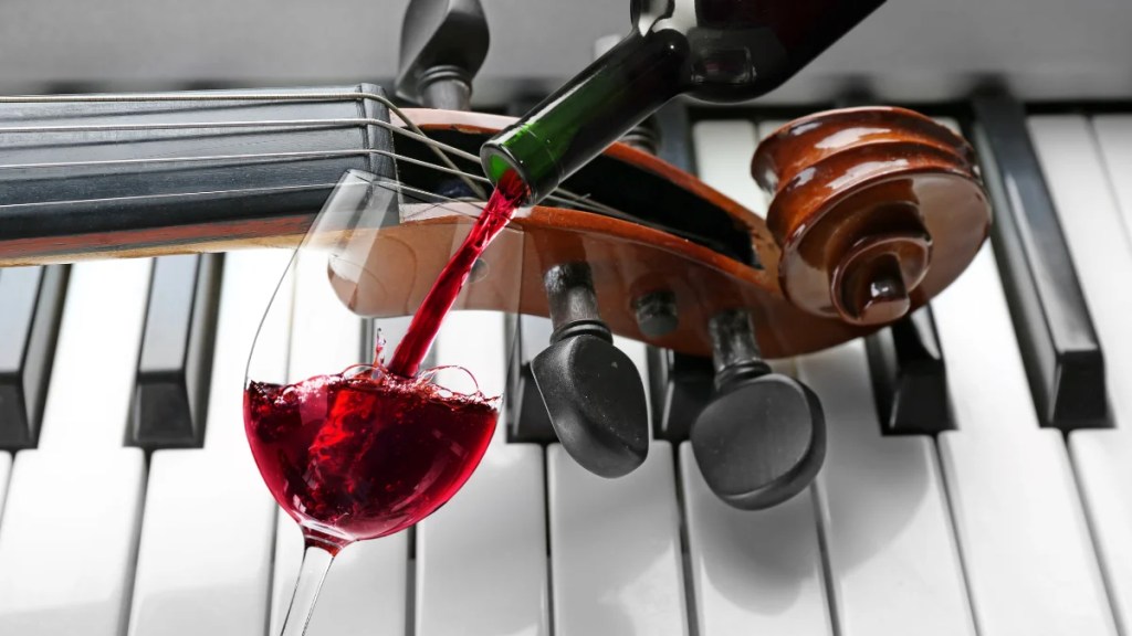 Red wine being poured into a glass in front of a violin and piano keys