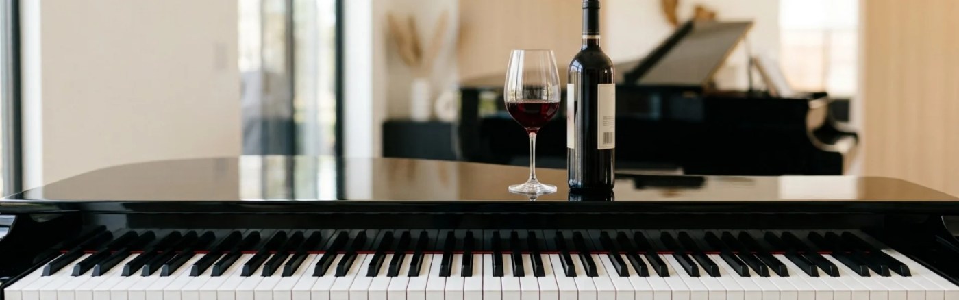 An elegant black grand piano keyboard with a glass and bottle of red wine on its polished surface, referencing famous composers who loved wine.